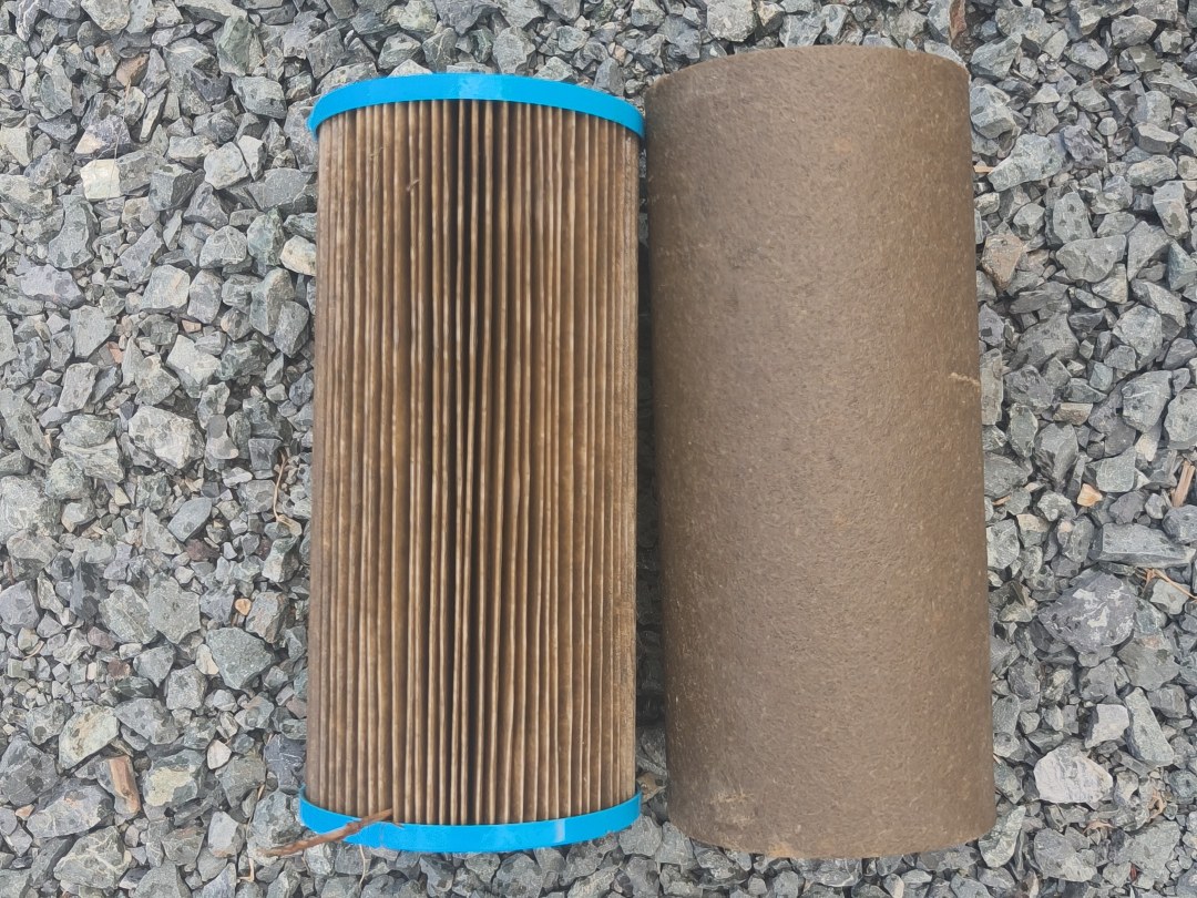 Two used rainwater filter cartridges side by side on gravel, heavily discoloured from sediment in a Mangawhai tank water system